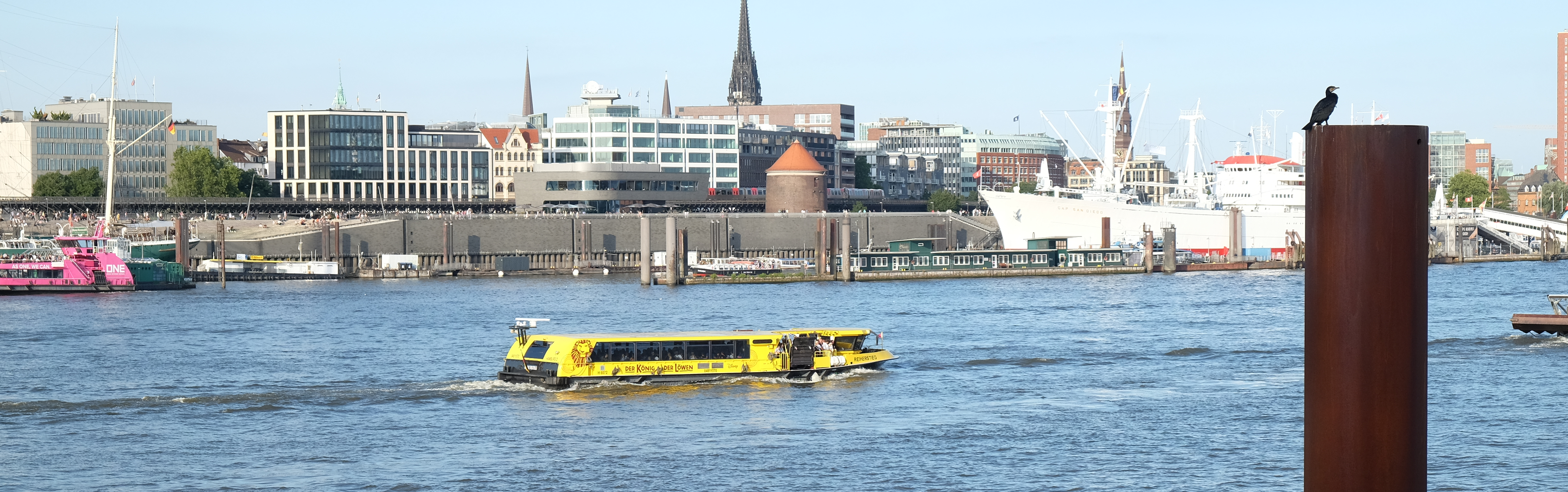 Blick auf die Landungsbrücken in Hamburg. Eine gelbe Barkasse schippert auf der Elbe.