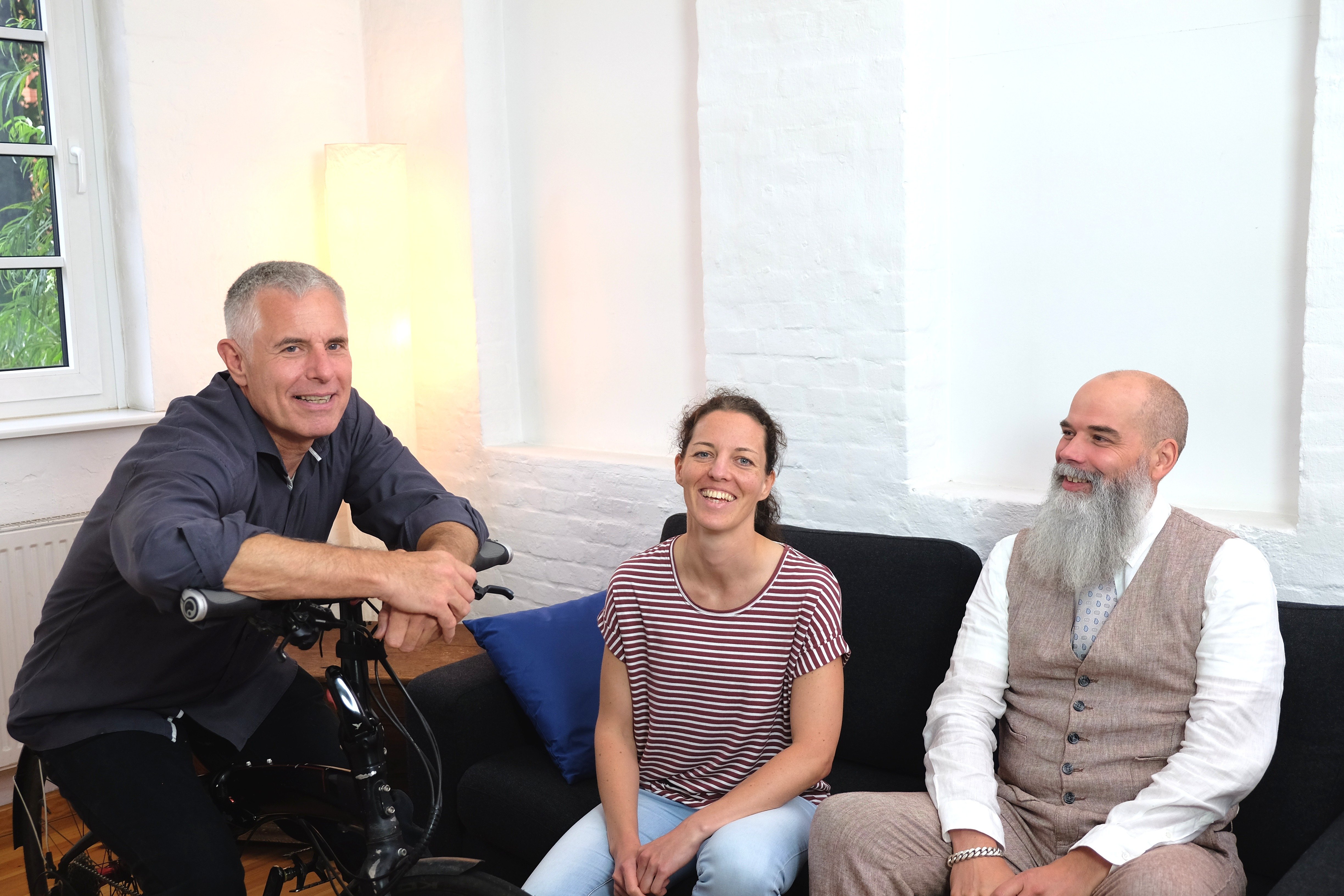 Rolf, Anne und Peer lachen sitzend auf Fahrrad bzw. Sofa. Es wirkt mega sympathisch :)