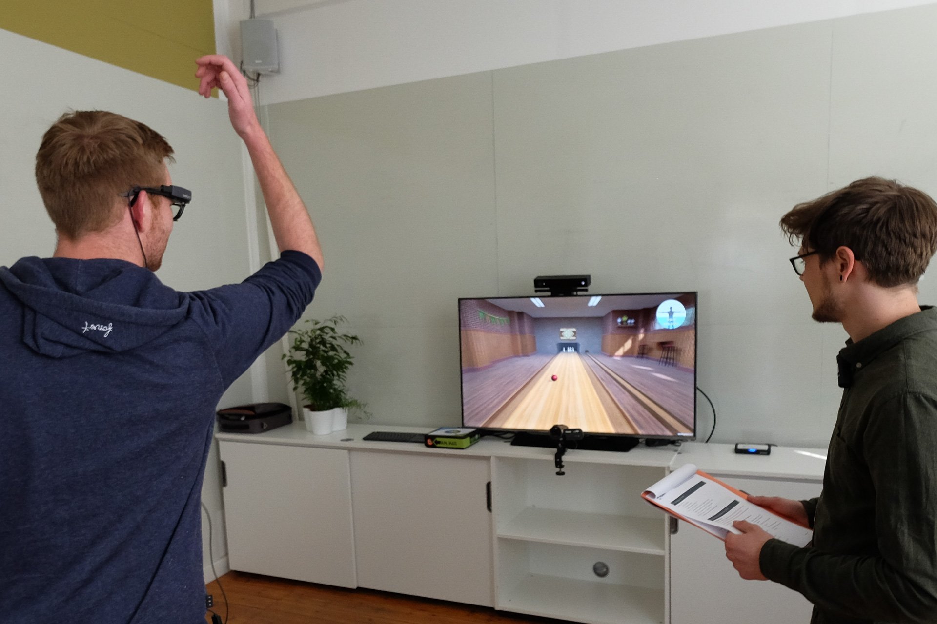 2 Menschen stehen vor Monitor und spielen virtuelles Bowling
