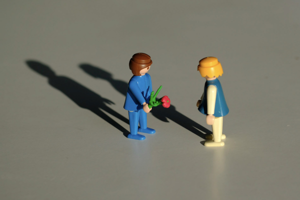 Nahaufnahme von 2 Playmobilfiguren, die sich gegenüberstehen. Die linke Figur hält eine rote Blume.