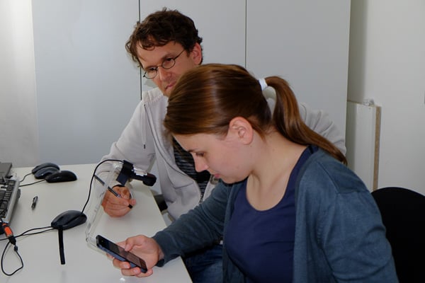 Interviewer schaut der Testperson über die Schulter während sie auf einem Handy etwas testet.